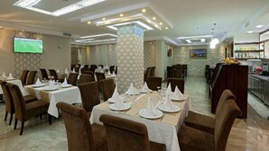 A restaurant with tables set for dining, a bar area, and a television screen on the wall. - Hôtel Saray (Algiers)