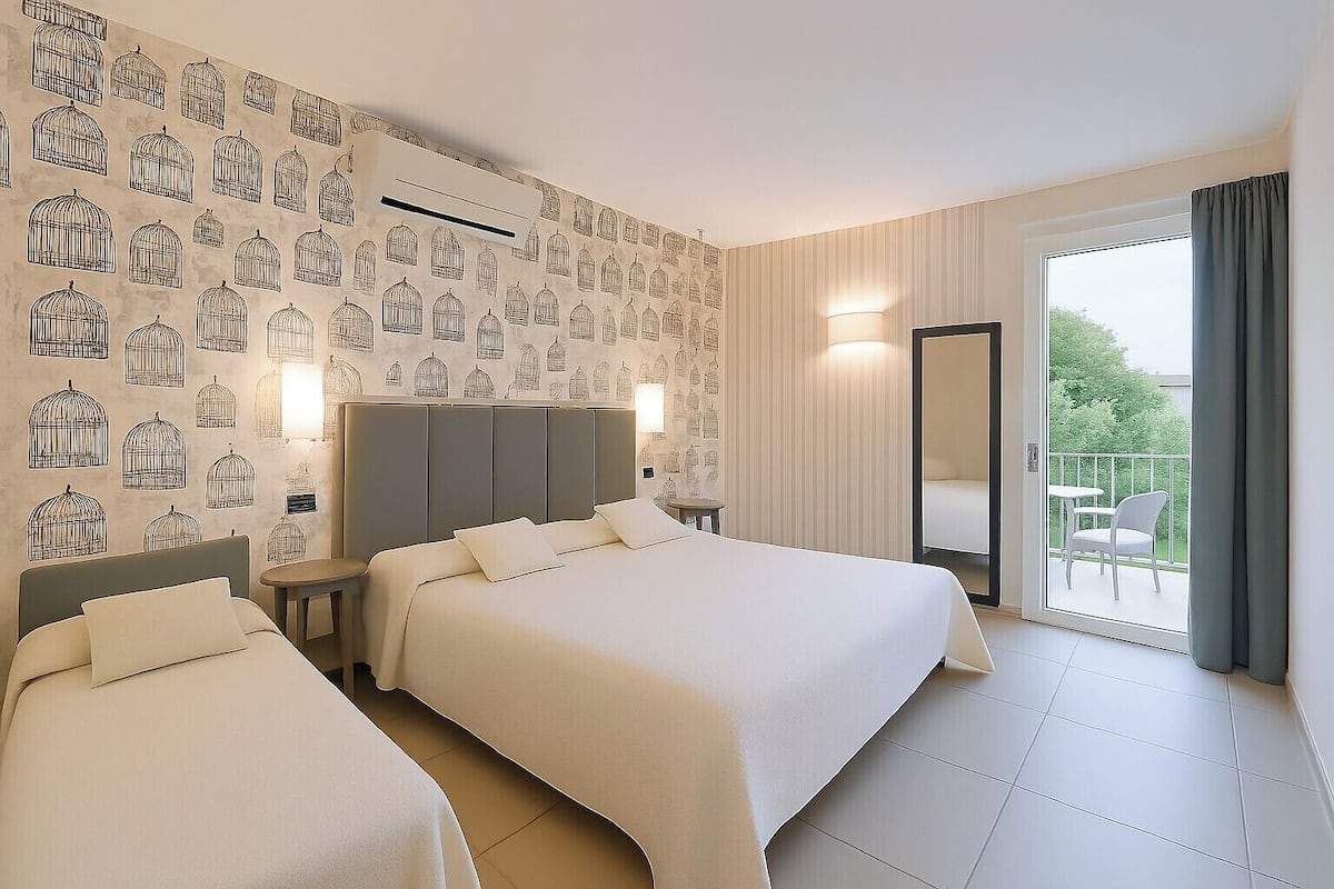 A hotel room with two beds, a large window with a view of greenery, and a balcony with a chair.