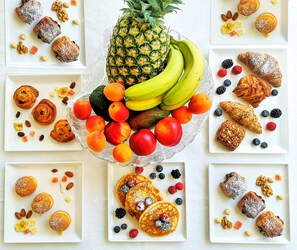 A fruit platter with bananas, pineapples, and various berries, surrounded by plates of pastries and muffins. - Hotel Darsena (Riccione)