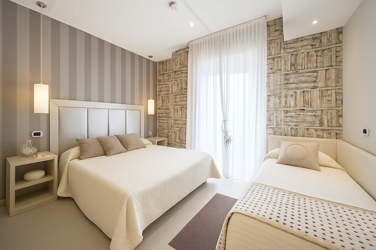 A modern hotel room with a large bed, bedside tables, and a stone-textured wall.