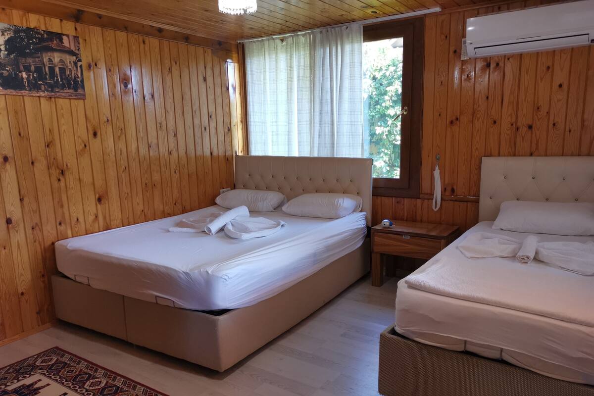 A wooden-paneled room with two beds, a bedside table, a nightstand, a patterned rug, and an air conditioning unit.