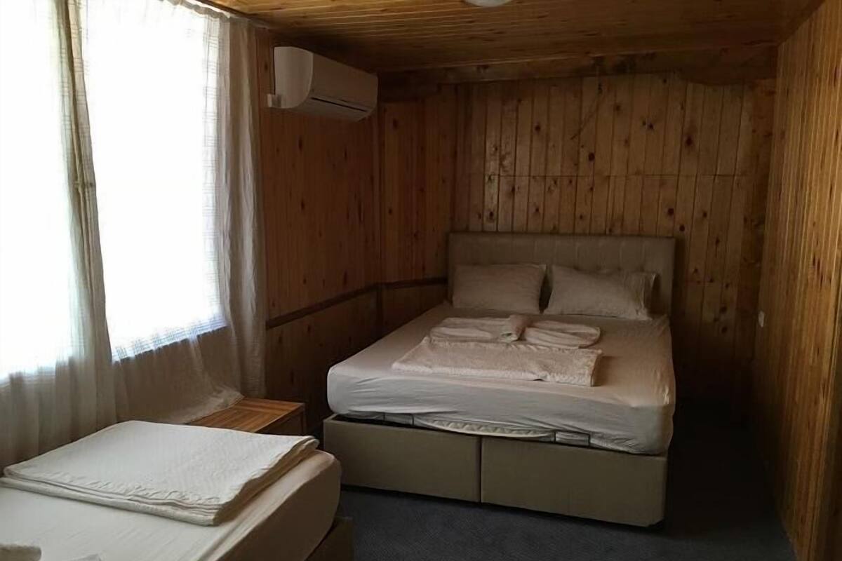 A wooden room with a bed, a small table, and a window with curtains.