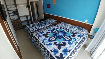 Quarto com duas camas, um guarda-roupa e uma porta que dá para outro espaço.