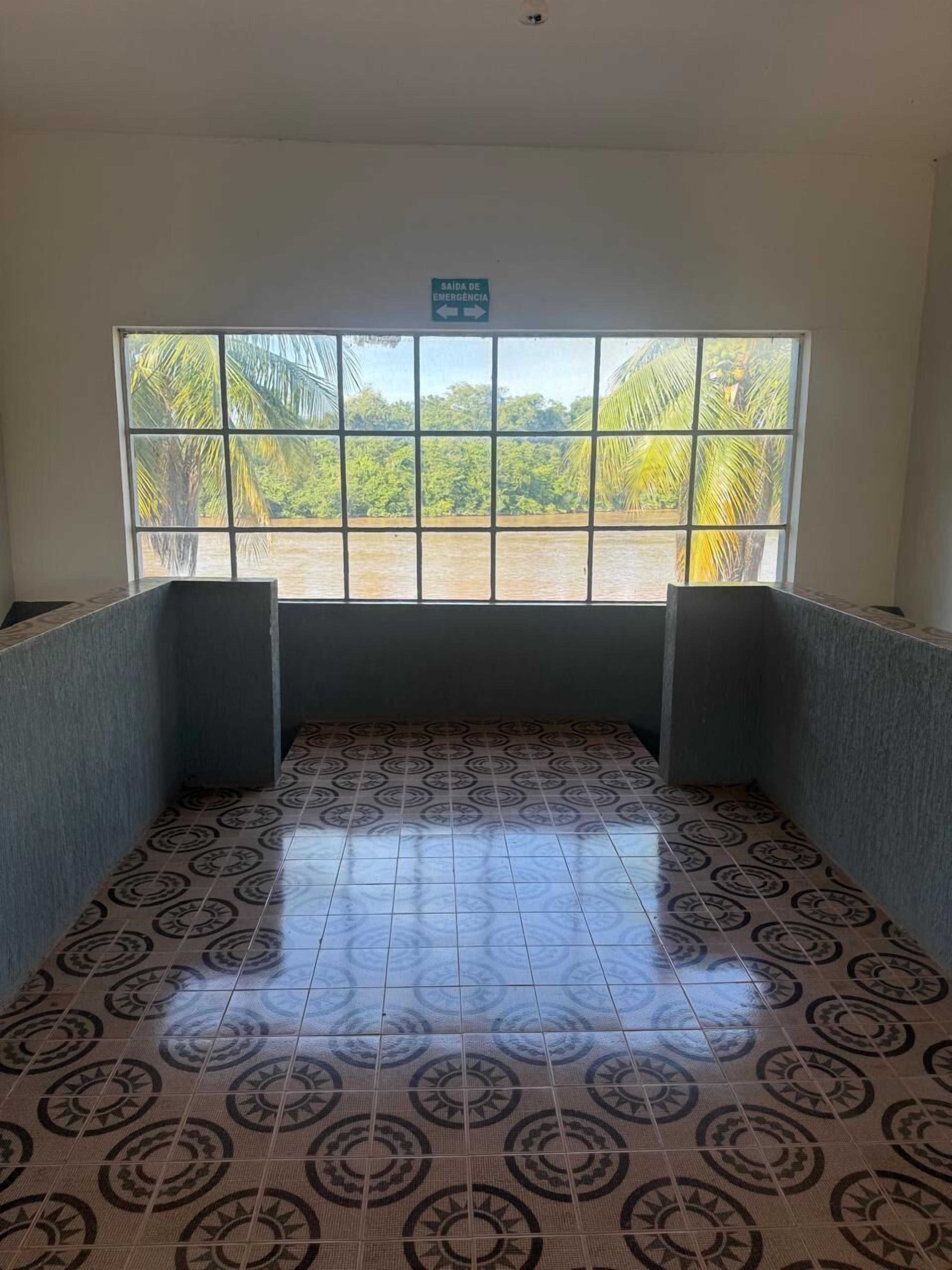 A room with a patterned floor, a window with a view of palm trees, and a sign indicating an emergency exit.