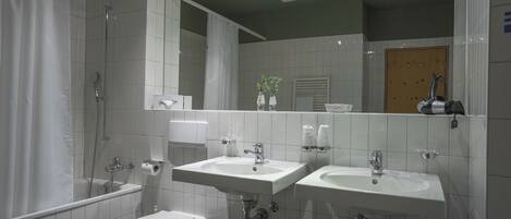 A modern bathroom with two sinks, a shower, a toilet, and a mirror.