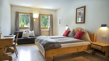 A bedroom with a wooden bed, a desk, a chair, a sofa, and a window with curtains.