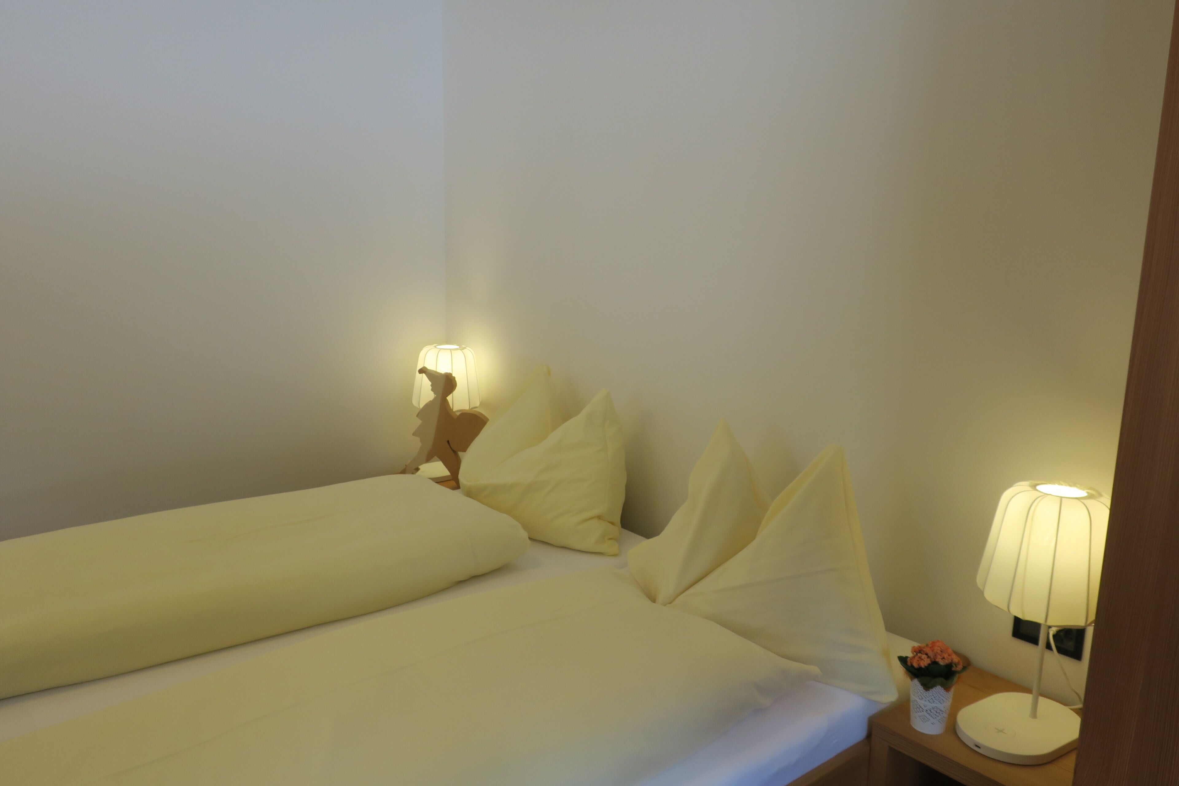 Ein ordentlich bezogenes Bett mit Kissen, ein Nachttisch mit Lampe und eine Blumenvase.