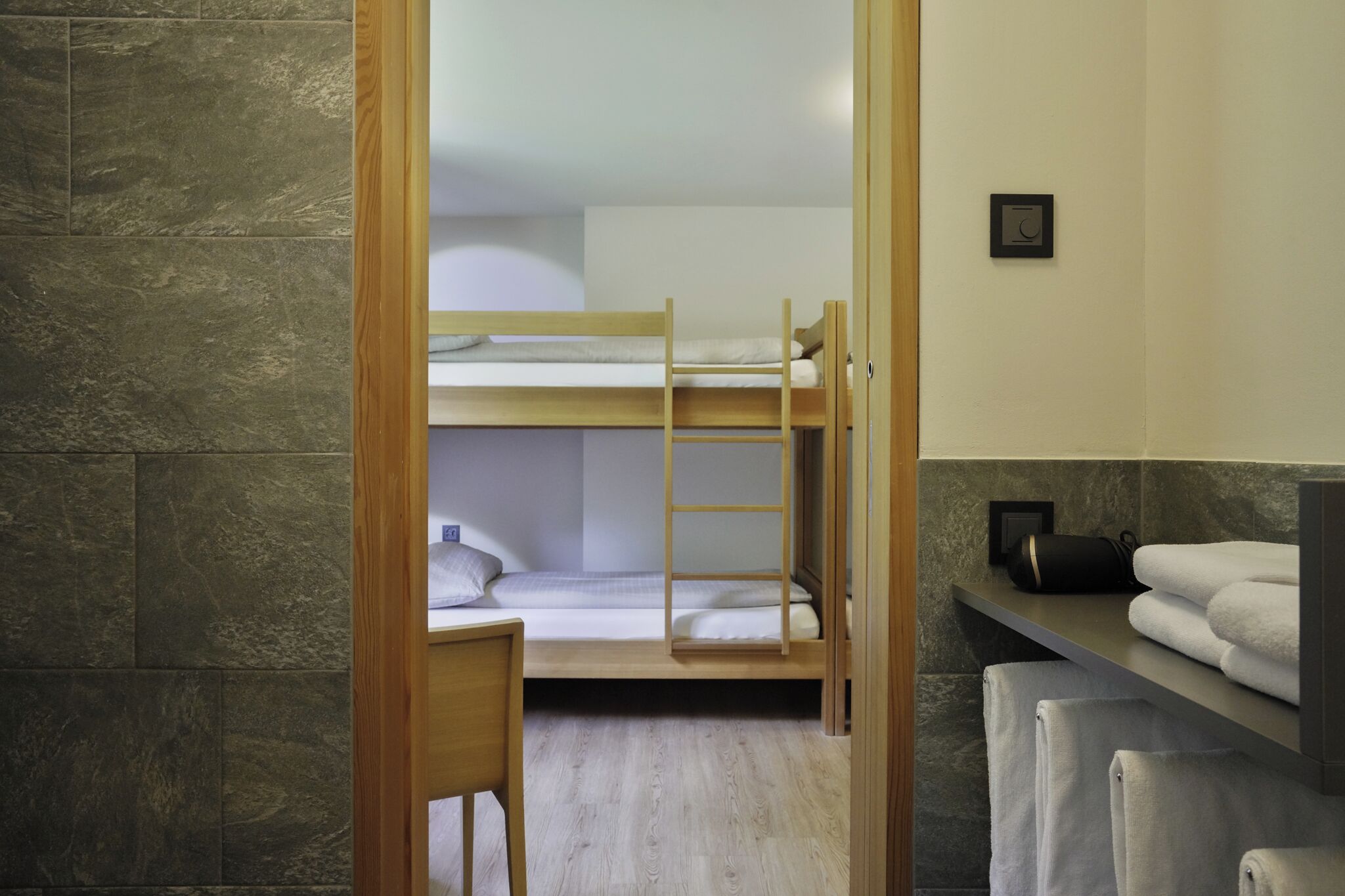 A bunk bed room with a wooden ladder, a small desk, and a shelf with towels.