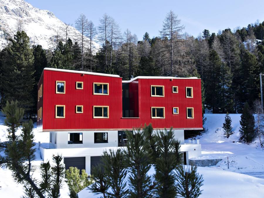 Un edificio rojo y blanco con muchas ventanas, rodeado de nieve y árboles.