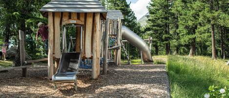 Un parque infantil con tobogán y estructuras para escalar, rodeado de árboles y un sendero de grava.