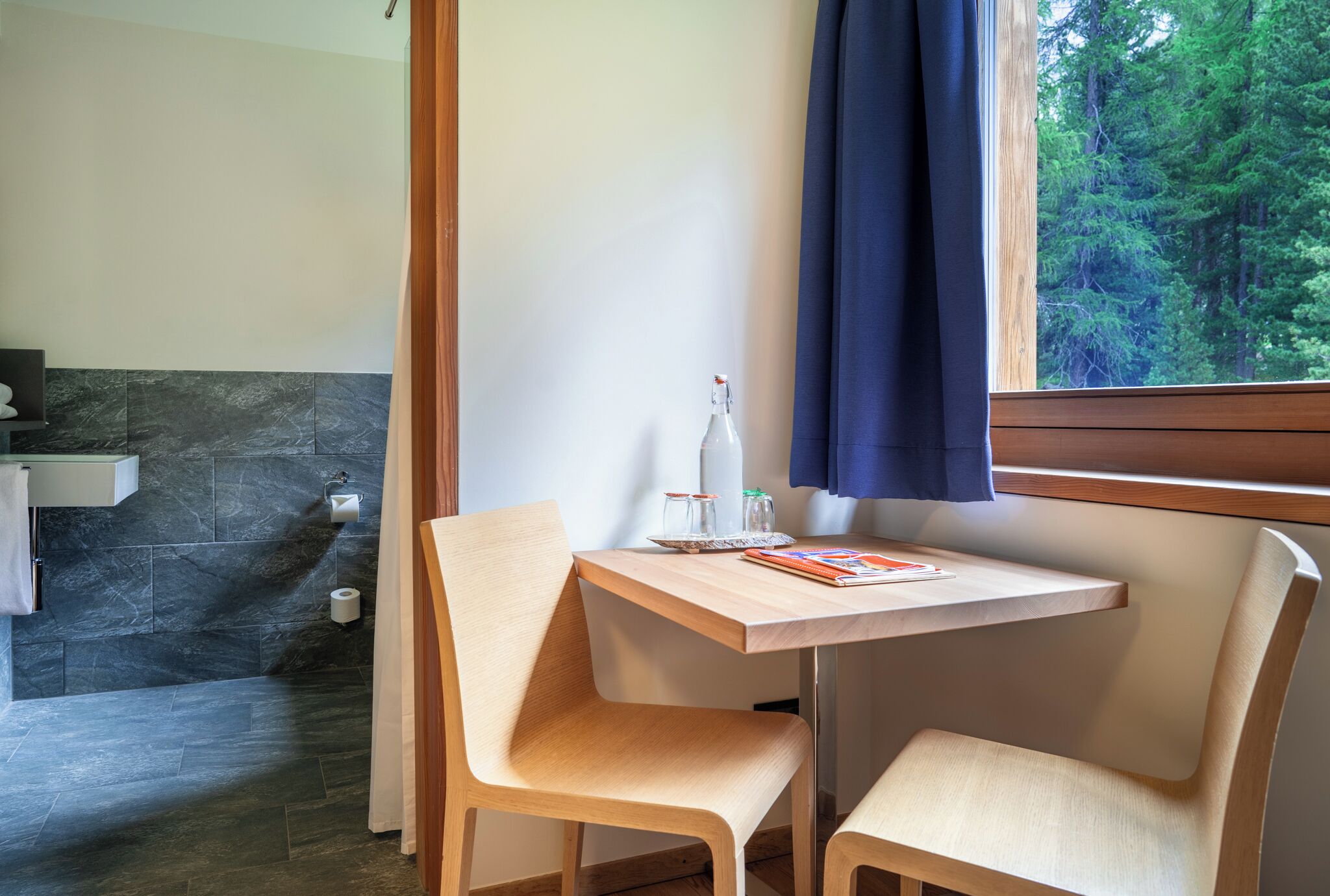 A bathroom with a shower, a sink, and a window with a view of trees.