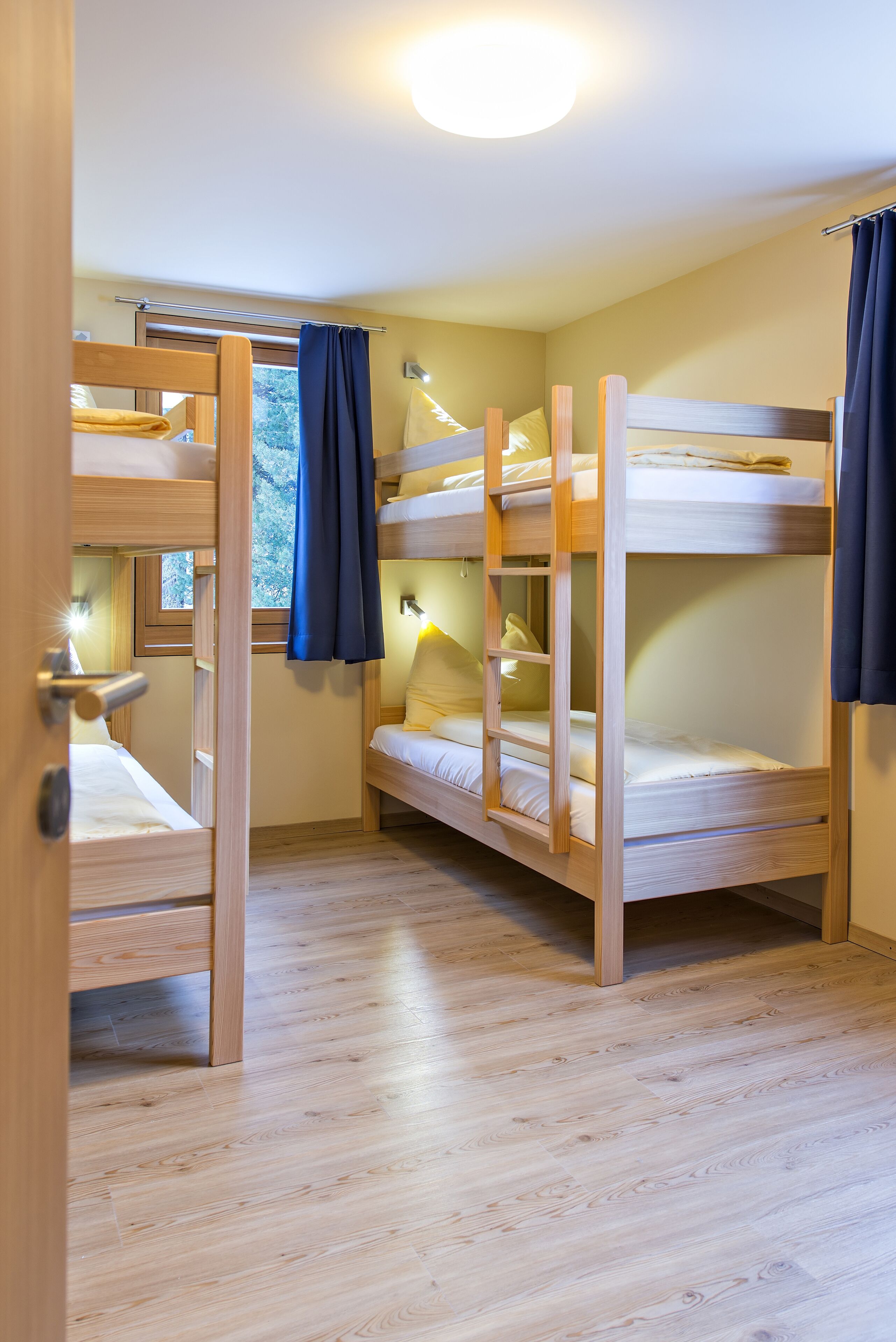 Een kamer met stapelbedden, houten vloer en een raam met gordijnen.