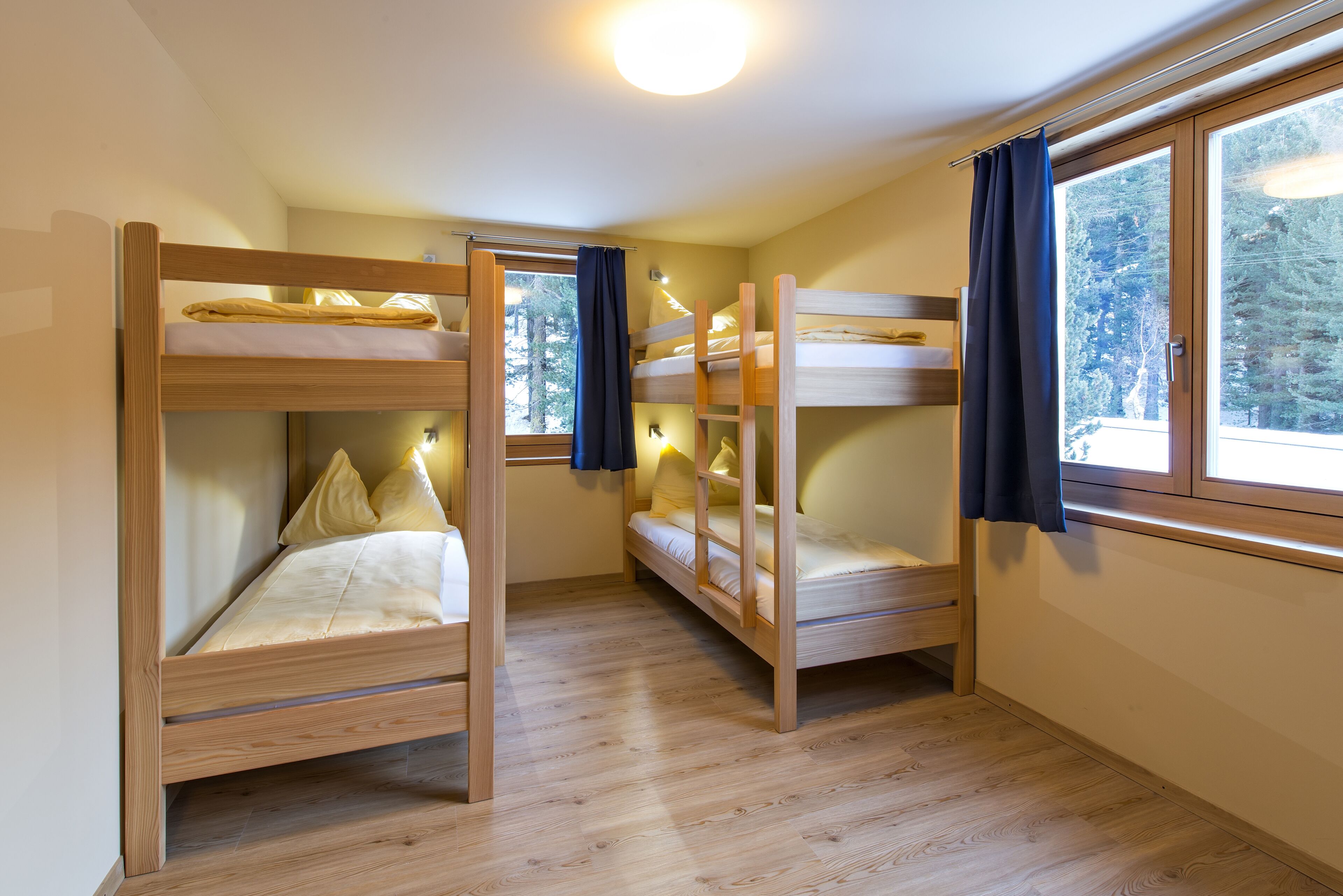 Una habitación con tres literas, piso de madera y ventanas grandes con cortinas.