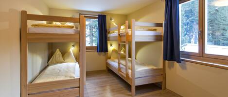 Una habitación con tres literas, piso de madera y ventanas grandes con cortinas.