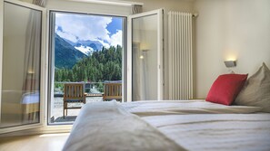 A bedroom with a bed, a red pillow, and a view of a mountain landscape through a glass door. - Hotel Morteratsch (Pontresina)