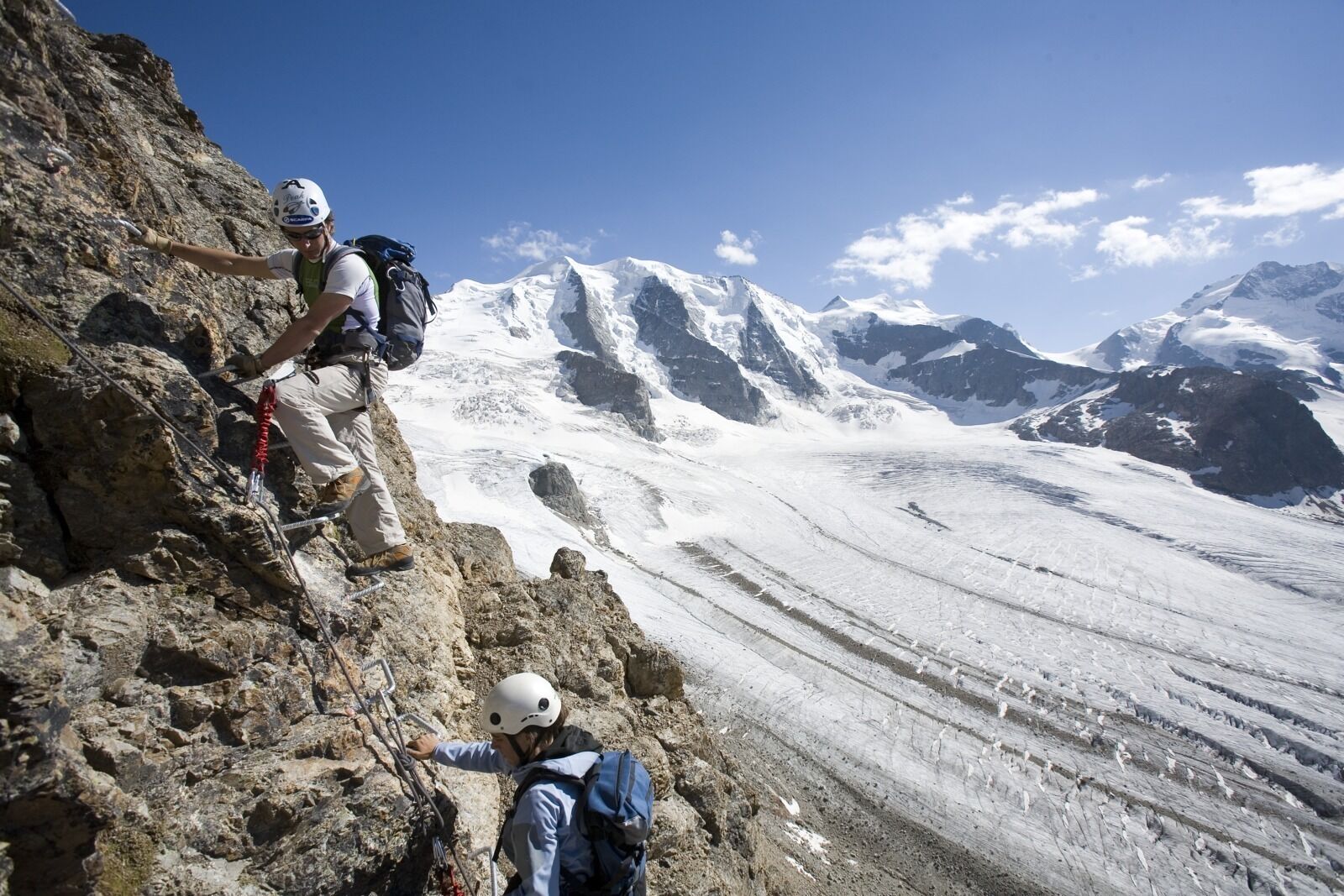 Terreno montuoso roccioso con scalatori e un ghiacciaio.