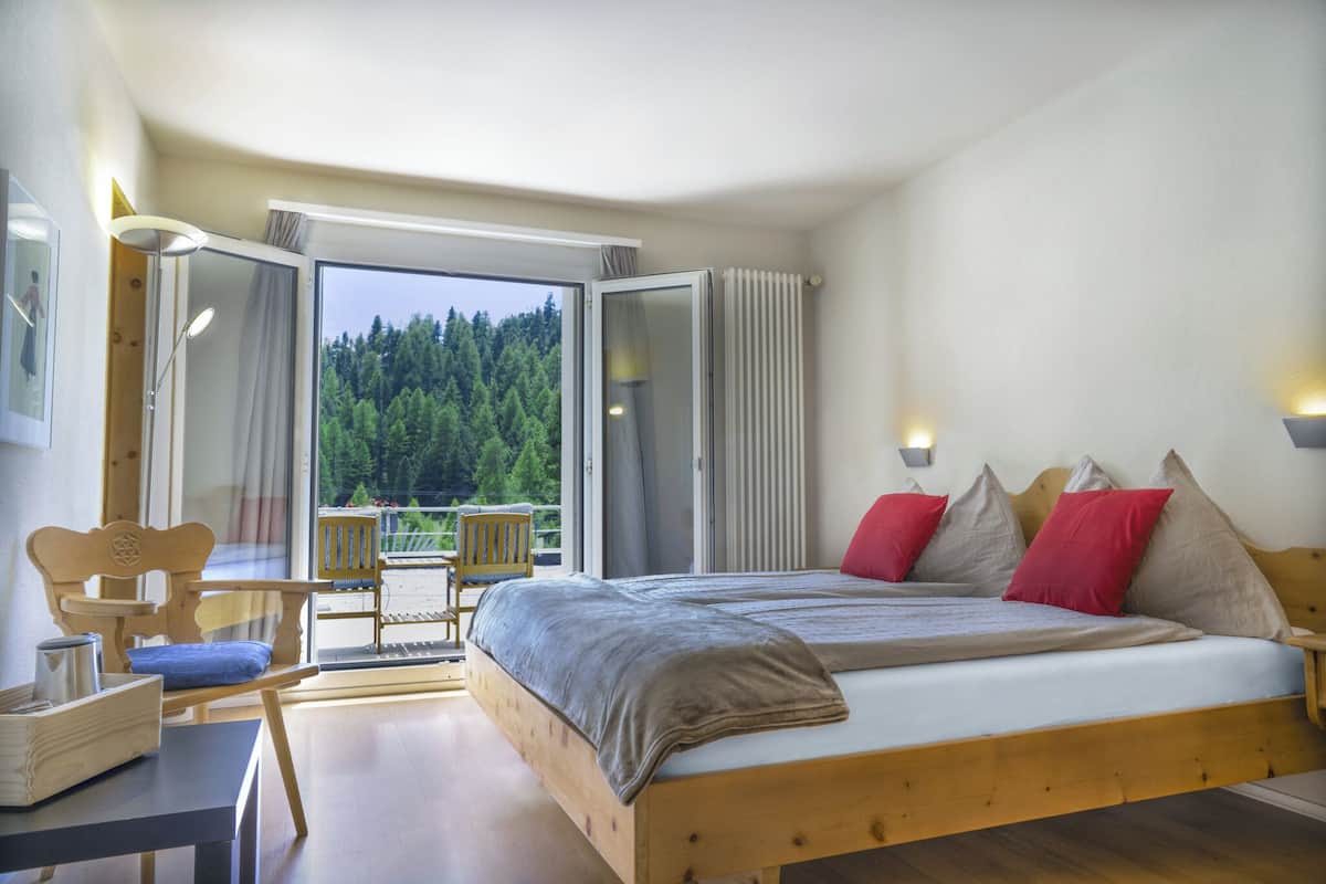 A bedroom with a wooden bed, a desk, and a chair. There is a large window with a view of trees.