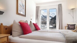 A bedroom with a large bed, wooden headboard, and a view of snow-capped mountains through a sliding door. - Hotel Morteratsch (Pontresina)