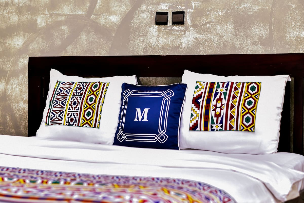 A bed with patterned pillows and a blue pillow with a letter 'M'.