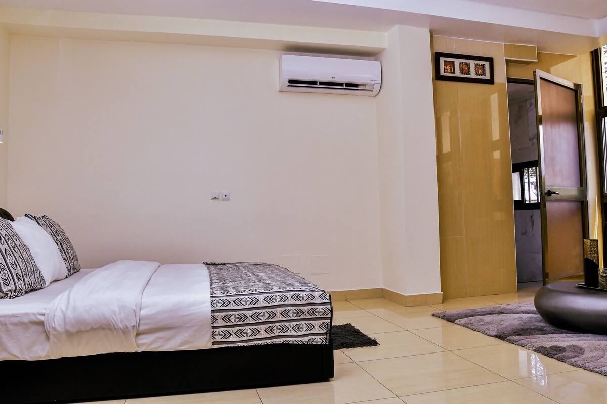 A bedroom with a bed, an air conditioning unit, a door, and a window.