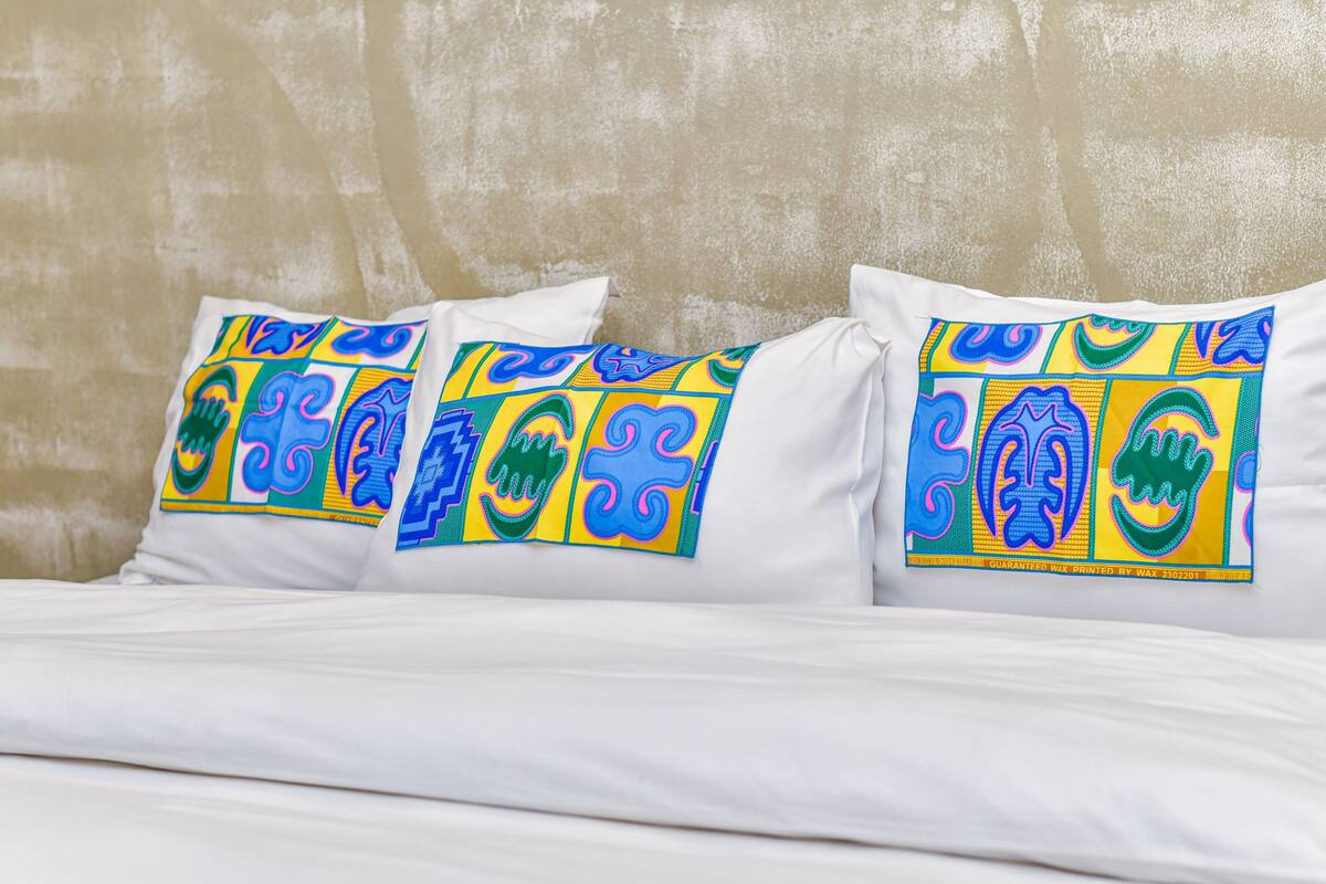 A bed with white bedding and colorful pillows featuring abstract designs.