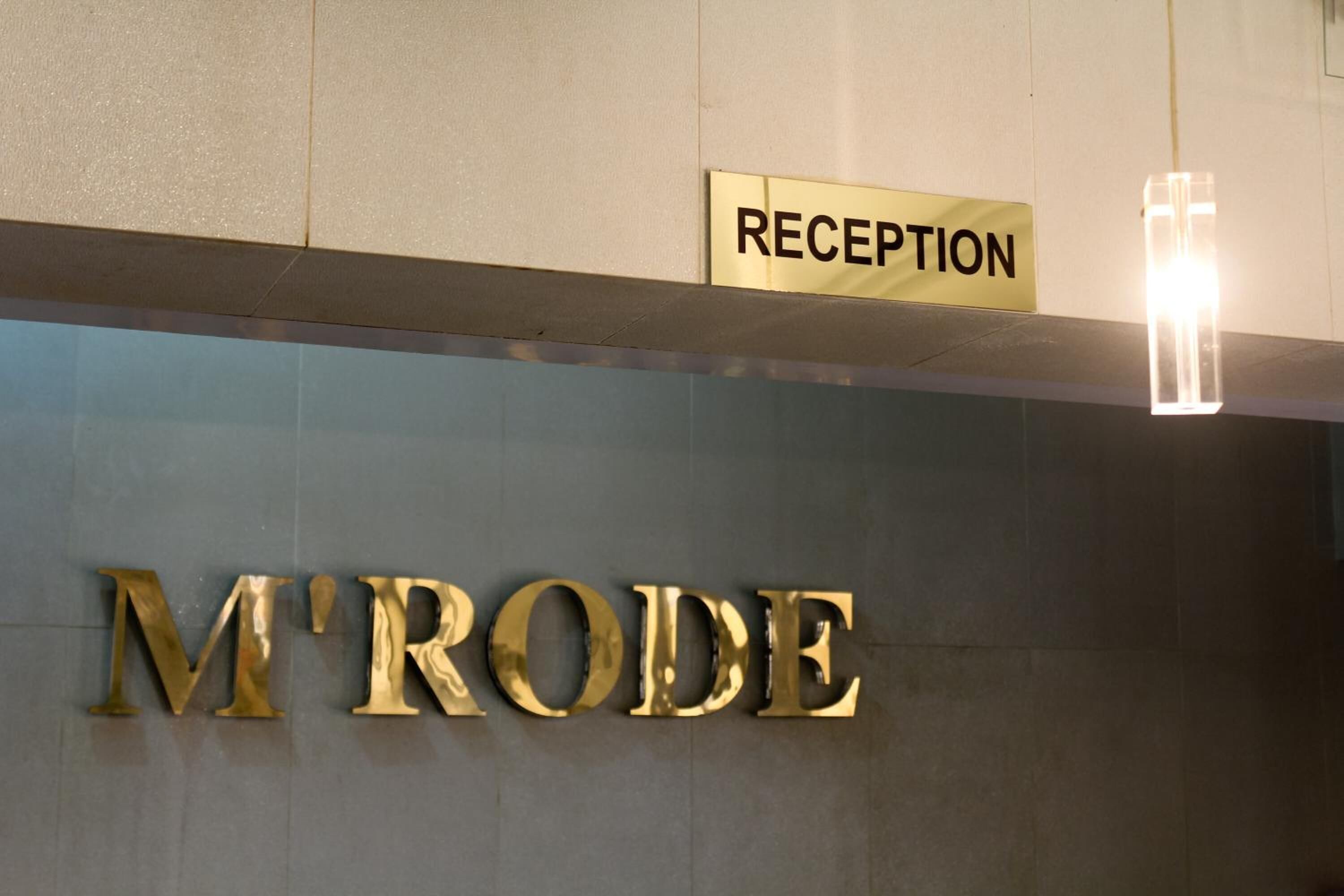 Un cartel de recepción y el nombre 'M'TRODE' en letras doradas grandes sobre una pared.