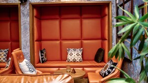 A seating area with orange leather sofas and cushions, a small round table, and a patterned wall. - Hotel M'Rode (Lomé)