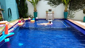 A swimming pool with two people in the water, surrounded by various colorful floating toys and potted plants. - Villa Sophia (São Paulo)