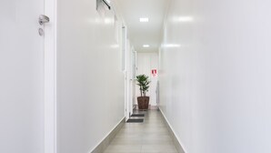 A clean, white hallway with a potted plant and a fire exit sign. - Villa Sophia (São Paulo)