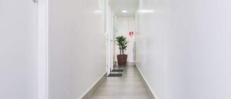 A clean, white hallway with a potted plant and a fire exit sign.