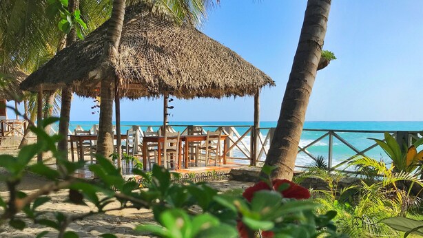 A beachside area with a thatched-roof structure, wooden chairs, and a view of the ocean. - Coterelle Breeze (Marigot)
