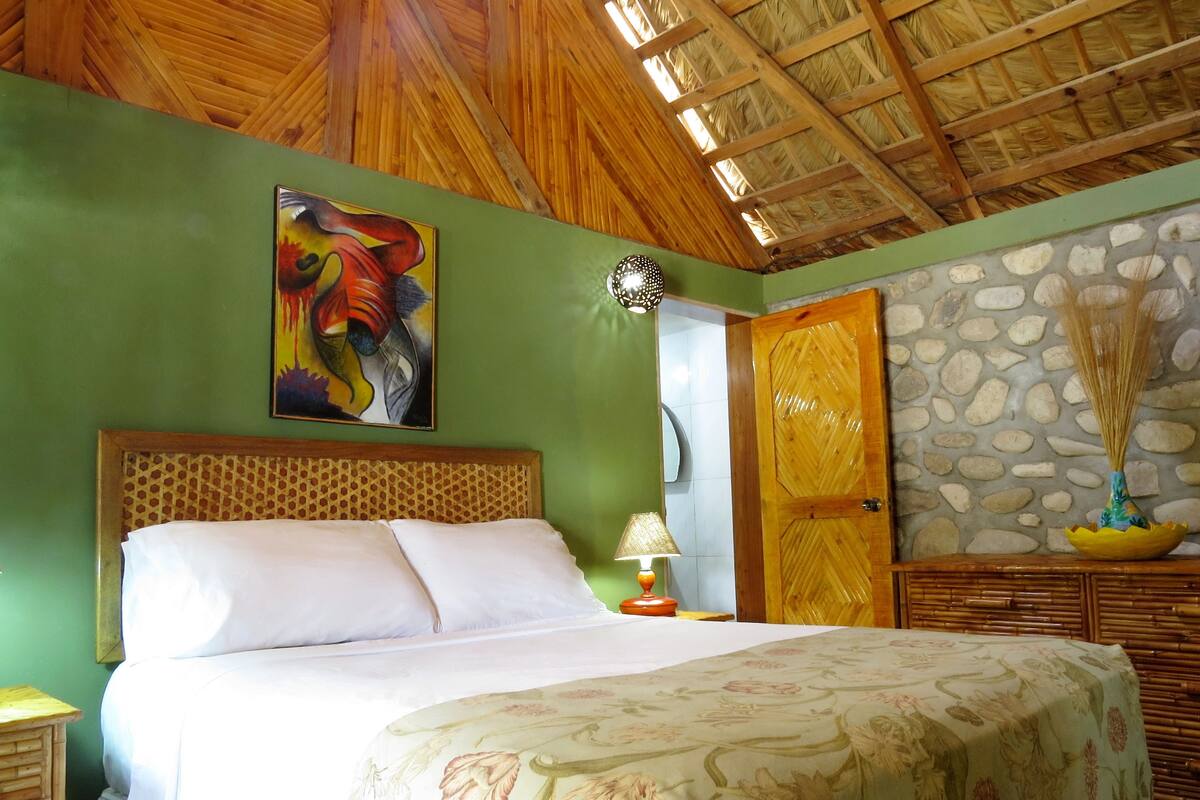 Une chambre à coucher avec un lit, un tableau, une lampe, un mur en pierre et une porte en bois.
