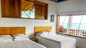 A room with two beds, wooden headboards, a window with a view of the sea, and a wooden cabinet above the beds. - Coterelle Breeze (Marigot)