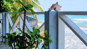 A beach view with a railing, palm trees, and a seashell. - Coterelle Breeze (Marigot)