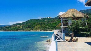 A beachside resort with a thatched-roof structure, clear blue waters, and a hilly backdrop. - Coterelle Breeze (Marigot)