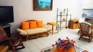 A living room with a sofa, a coffee table with a floral arrangement, a TV, and a bookshelf. - Casa en Marina Cid (Mazatlán)
