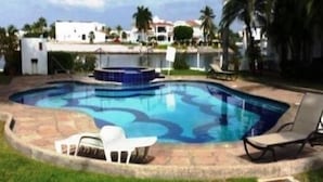 A swimming pool with a stone deck, surrounded by grass and palm trees. - Casa en Marina Cid (Mazatlán)