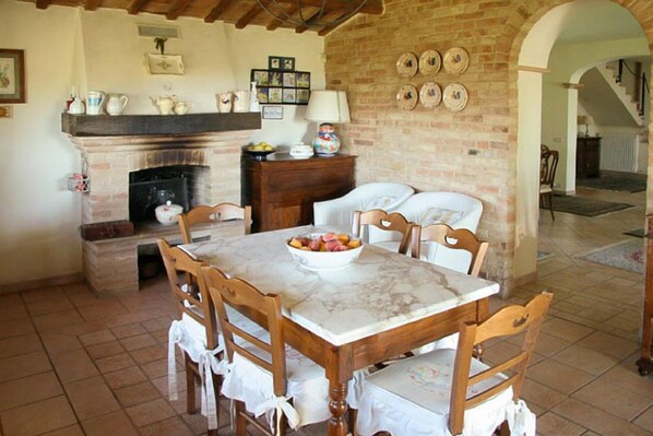 Un comedor con una mesa de mármol y sillas de madera, una chimenea de ladrillo y una pared de ladrillo decorada con placas.