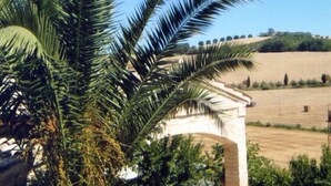 A patio area with a stone archway, outdoor seating, and a view of a vineyard. - Villa Rondanella (Fermo)