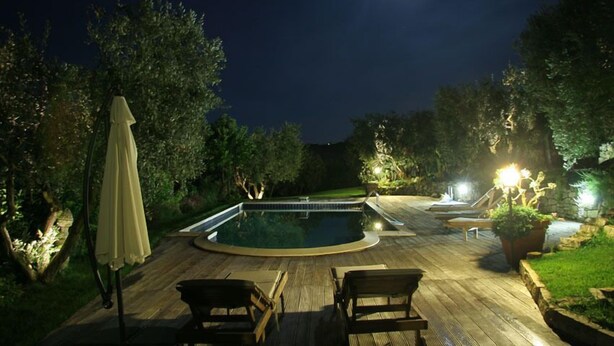 A nighttime outdoor swimming pool area with a wooden deck, lounge chairs, and a moonlit sky. - Villa Rondanella (Fermo)