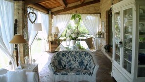 A cozy room with a wooden ceiling, a white cabinet with glass doors, a floral sofa, and a table with a vase of flowers. - Villa Rondanella (Fermo)