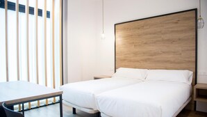 A modern hotel room with two single beds, a wooden headboard, a desk, and a chair.