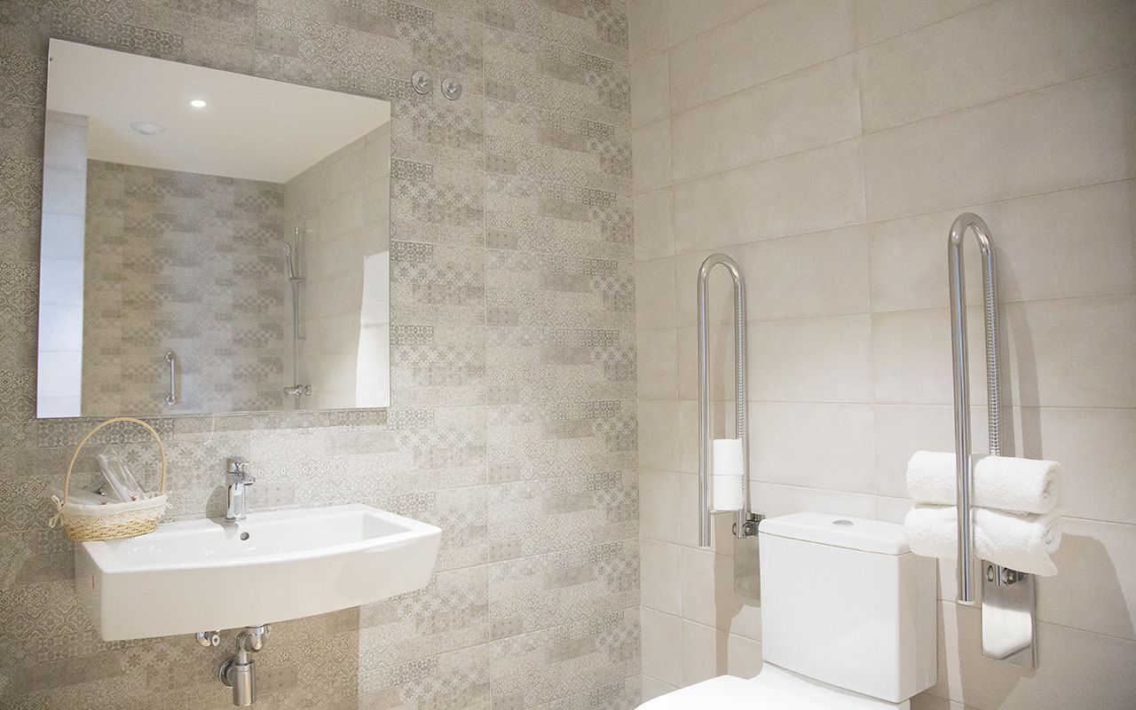 A bathroom with a sink, mirror, toilet, and grab bars.