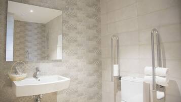 A bathroom with a sink, mirror, toilet, and grab bars.