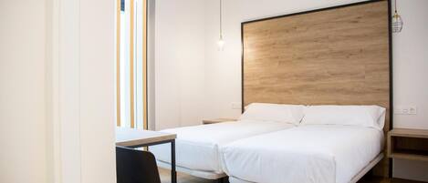 Una habitación de hotel con dos camas individuales, un escritorio con silla, cabecera de madera y lámpara colgante.