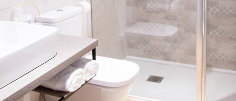 Un baño moderno con ducha envuelta en vidrio, inodoro blanco y tocador con barra para toallas.