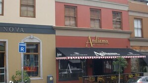 Een winkelgevel met een zwart luifel en een bord waarop 'Andiamo' staat, wat een restaurant, bar en delicatessenzaak aangeeft.