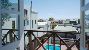 Een woongebouw met een balkon met uitzicht op een zwembad en omliggende huizen.
