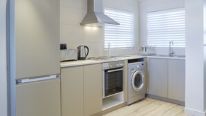 Een moderne keuken met een inbouwoven, magnetron en wasmachine, met lichtkleurige kastjes en een roestvrijstalen afzuigkap.