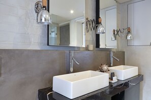 A modern bathroom with two white sinks, a large mirror, and pendant lights.
